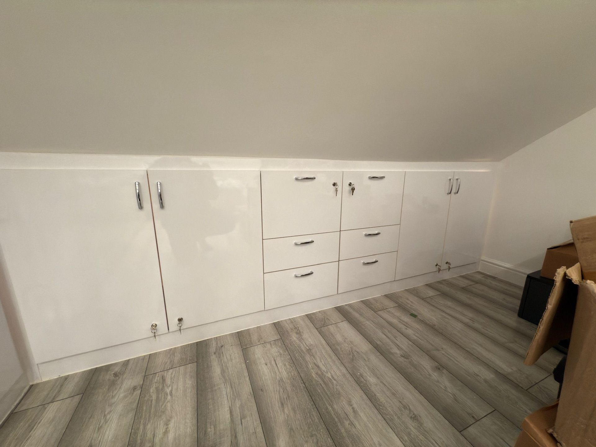 Gloss fitted eaves storage with drawers and lockable cupboards in a loft bedroom