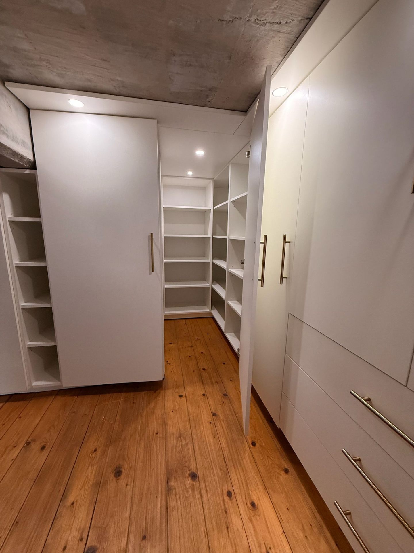 Walk-in wardrobe with open shelving system under concrete ceiling