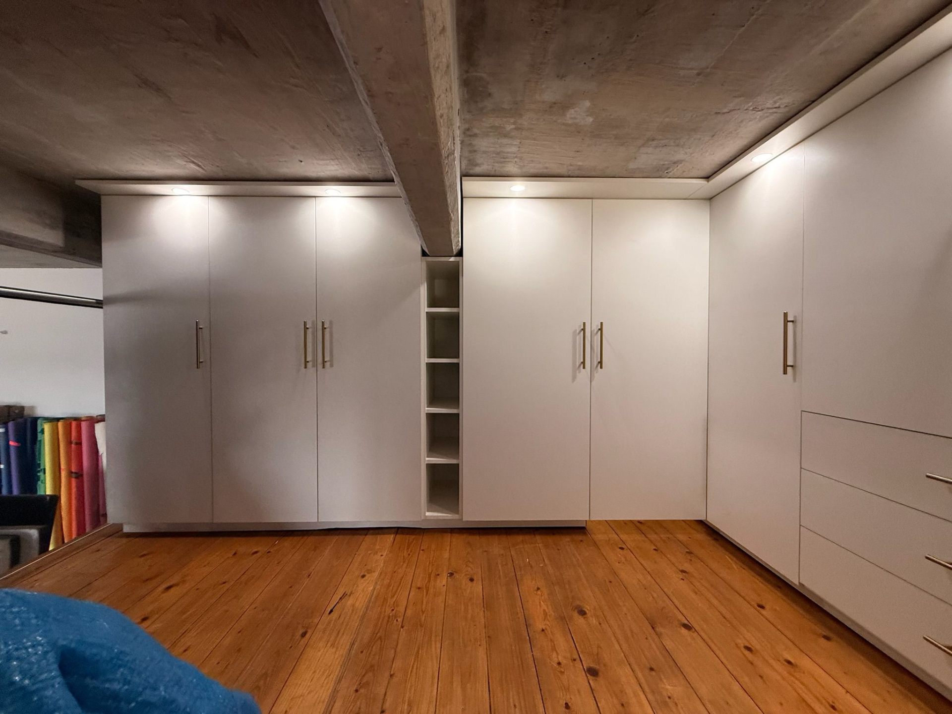 White fitted wardrobes with brass handles under exposed concrete ceiling
