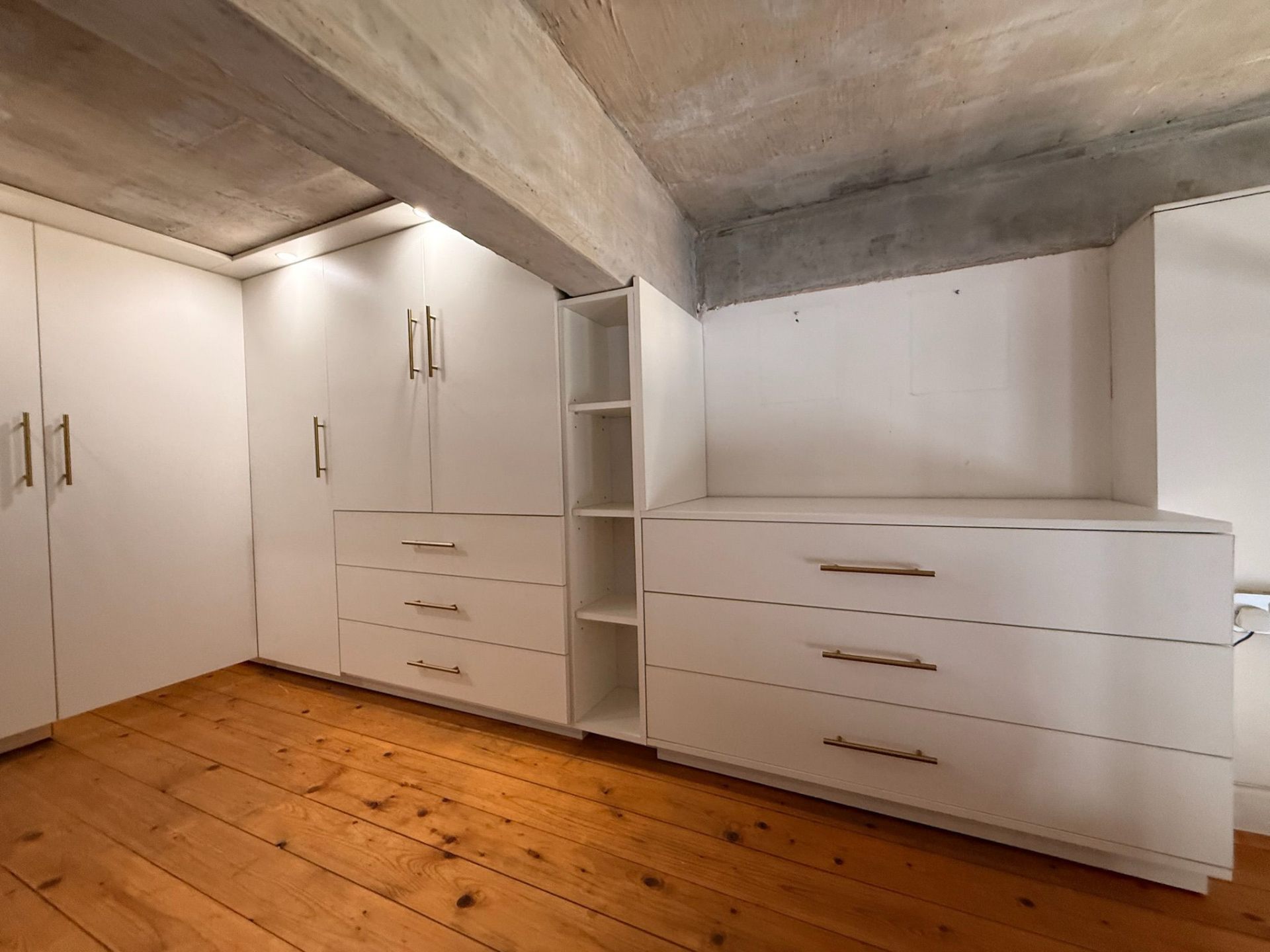 Corner view of white wardrobes with brass hardware in a loft walk-in